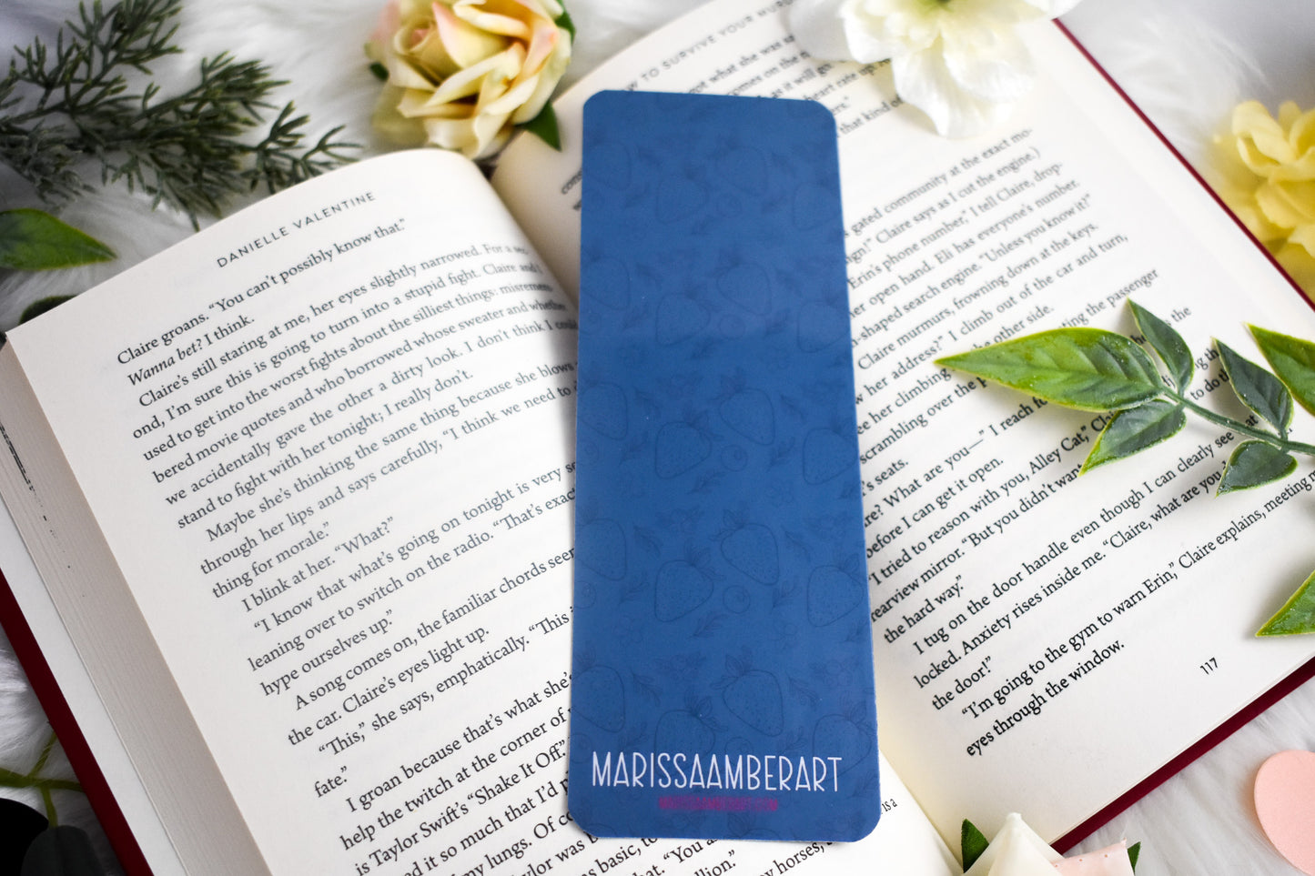 Blue bookmark with 'Marissa Amberart' branding on an open book with floral decorations.