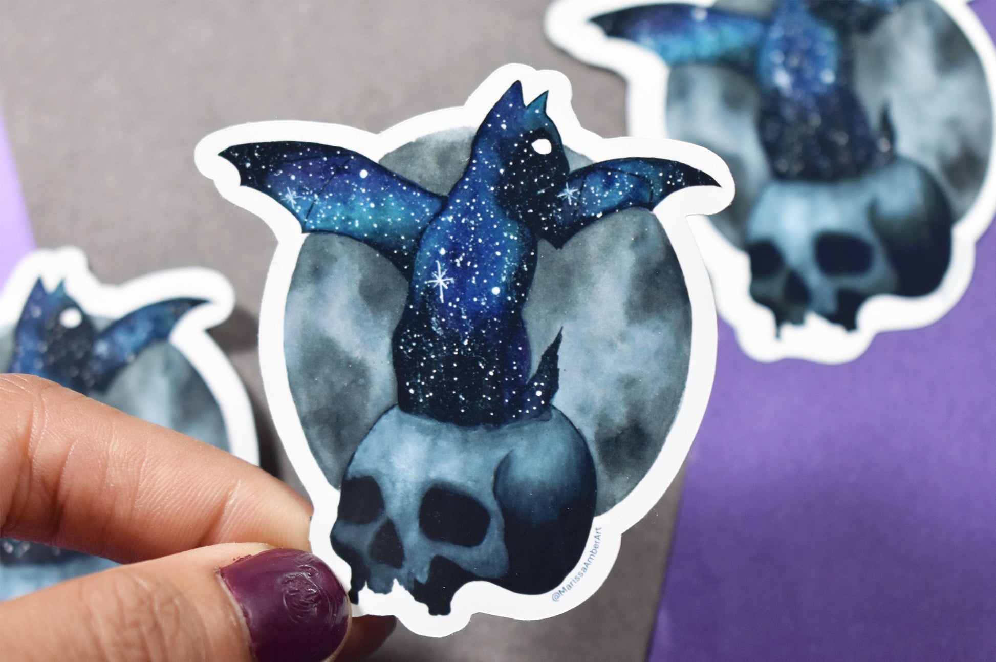 Sticker of a blue and black cat bat with starry sky design held by a hand.