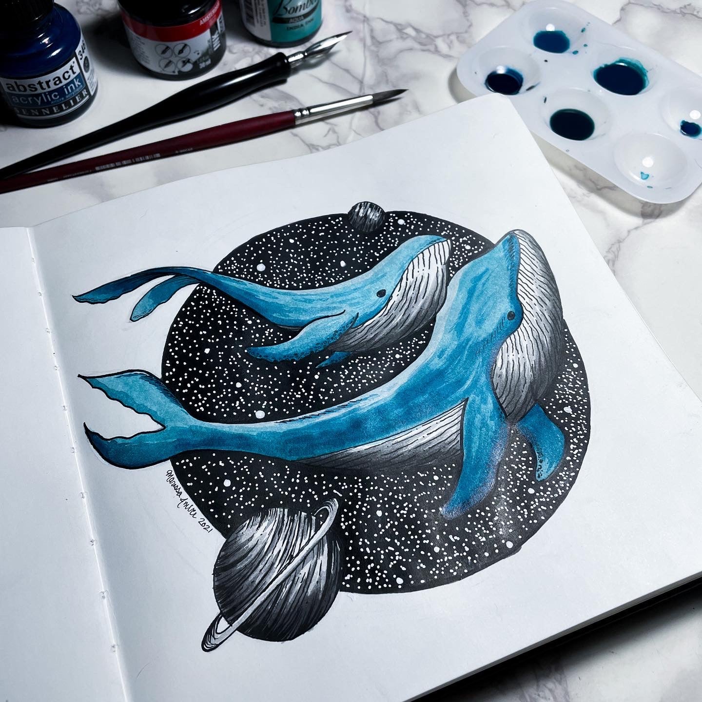Artistic depiction of whales with celestial elements on a piece of paper, surrounded by art supplies.