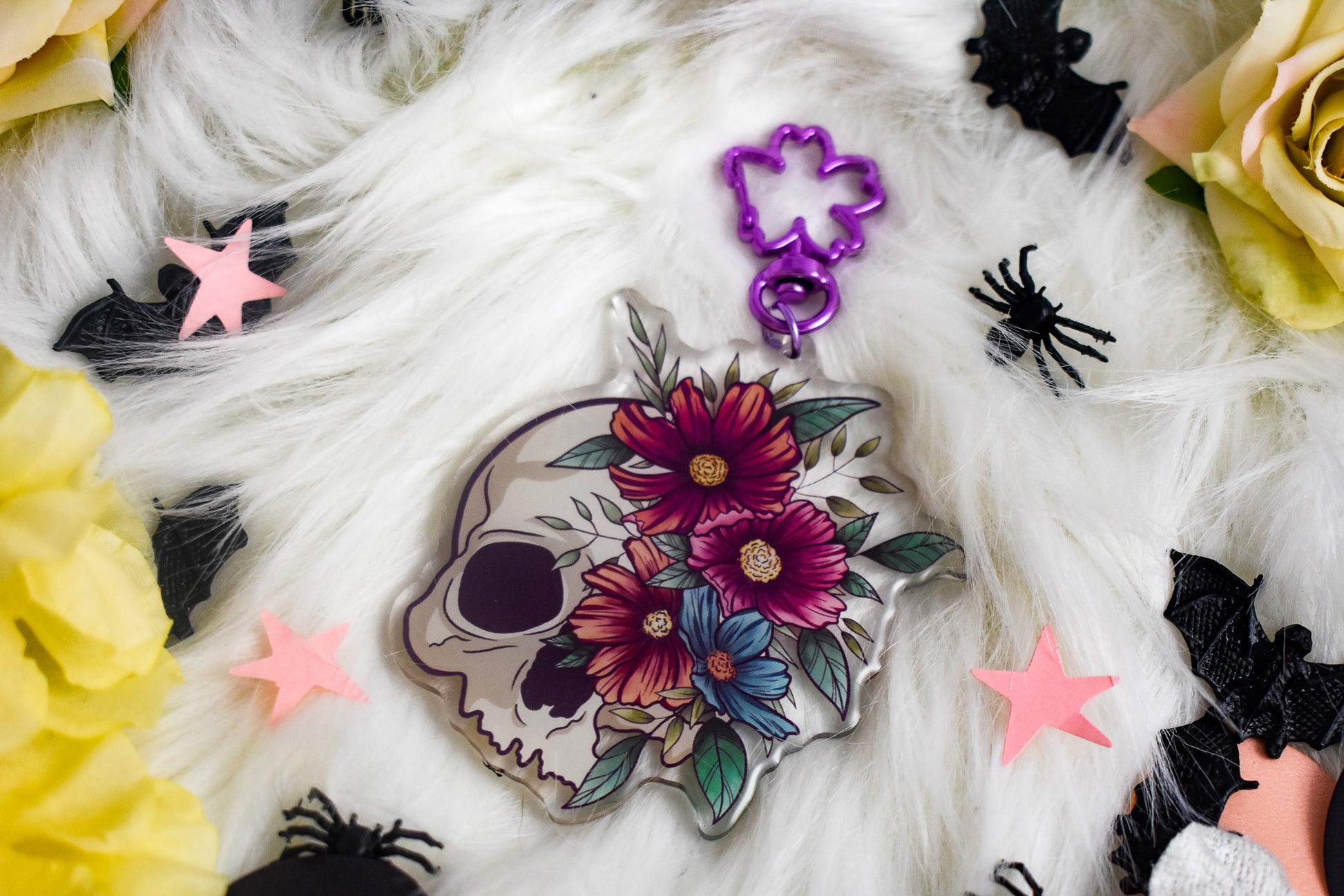 Decorative skull with floral design surrounded by colorful stars and spider decorations on a white surface.