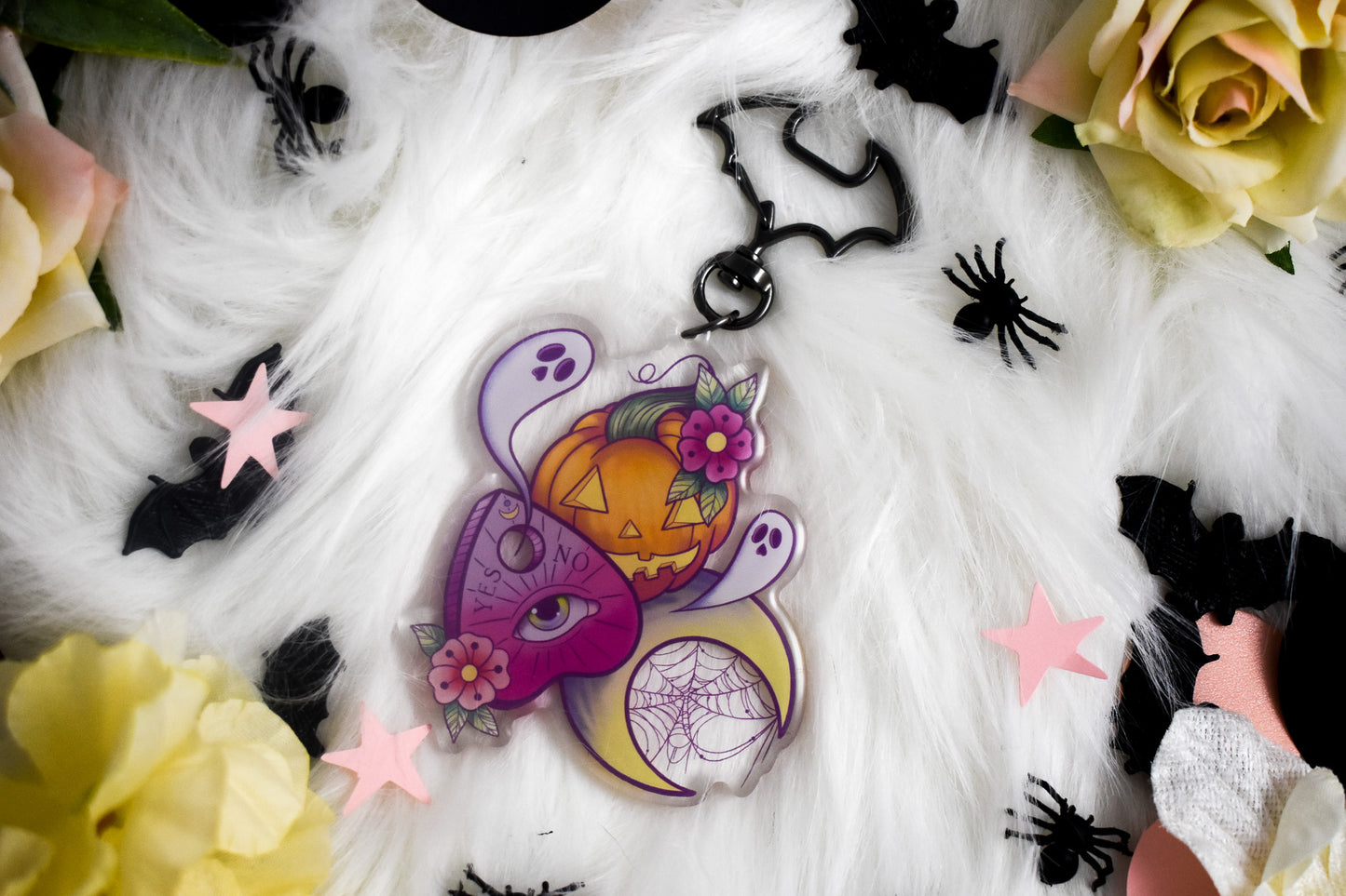 Decorative Halloween-themed keychain with pumpkins, flowers, and spider webs on a white fabric background.