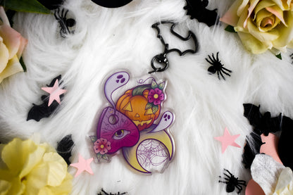 Decorative Halloween-themed keychain with pumpkins, flowers, and spider webs on a white fabric background.