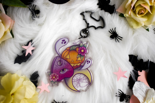 Decorative Halloween-themed keychain with pumpkins, flowers, and spider webs on a white fabric background.