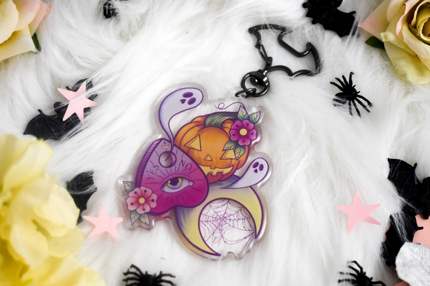 Decorative Halloween-themed keychain with pumpkins, flowers, and spider webs on a white fabric background.