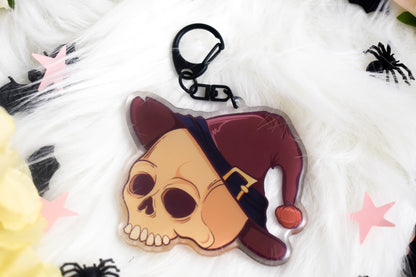 Skull-shaped keychain with a hat on a white background with spider decorations