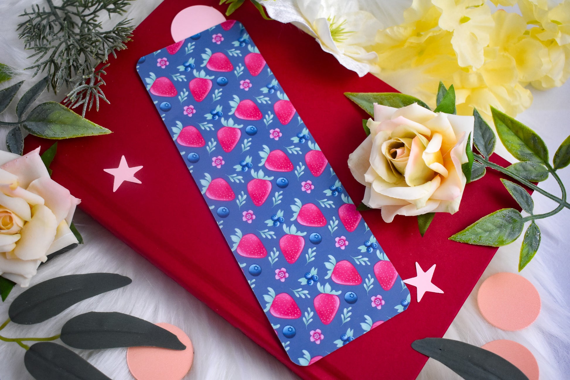 Blue bookmark with strawberry pattern on a red surface with flowers