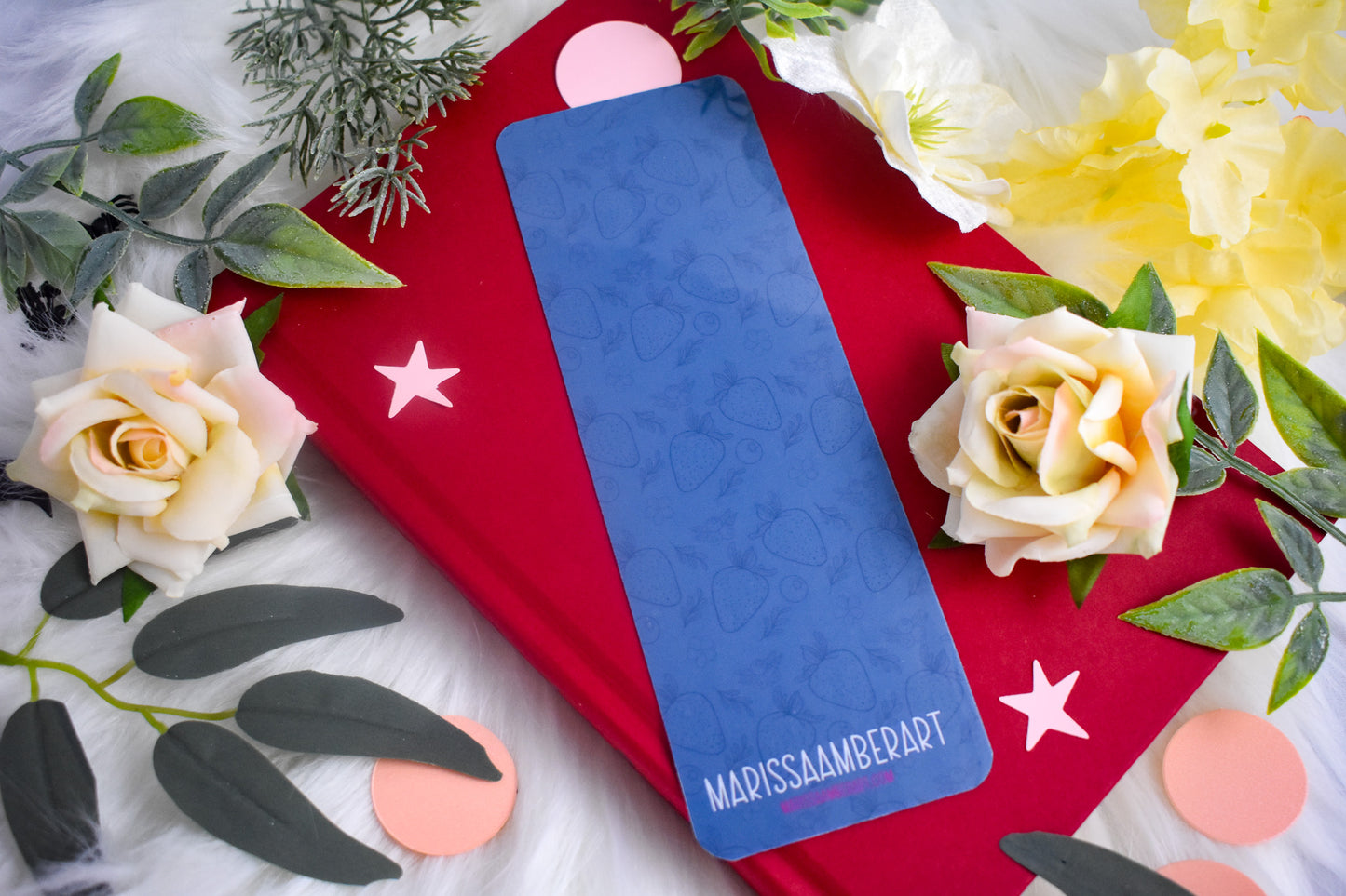 Blue bookmark with 'MarissaAmberArt' branding on a red book with flowers and leaves.