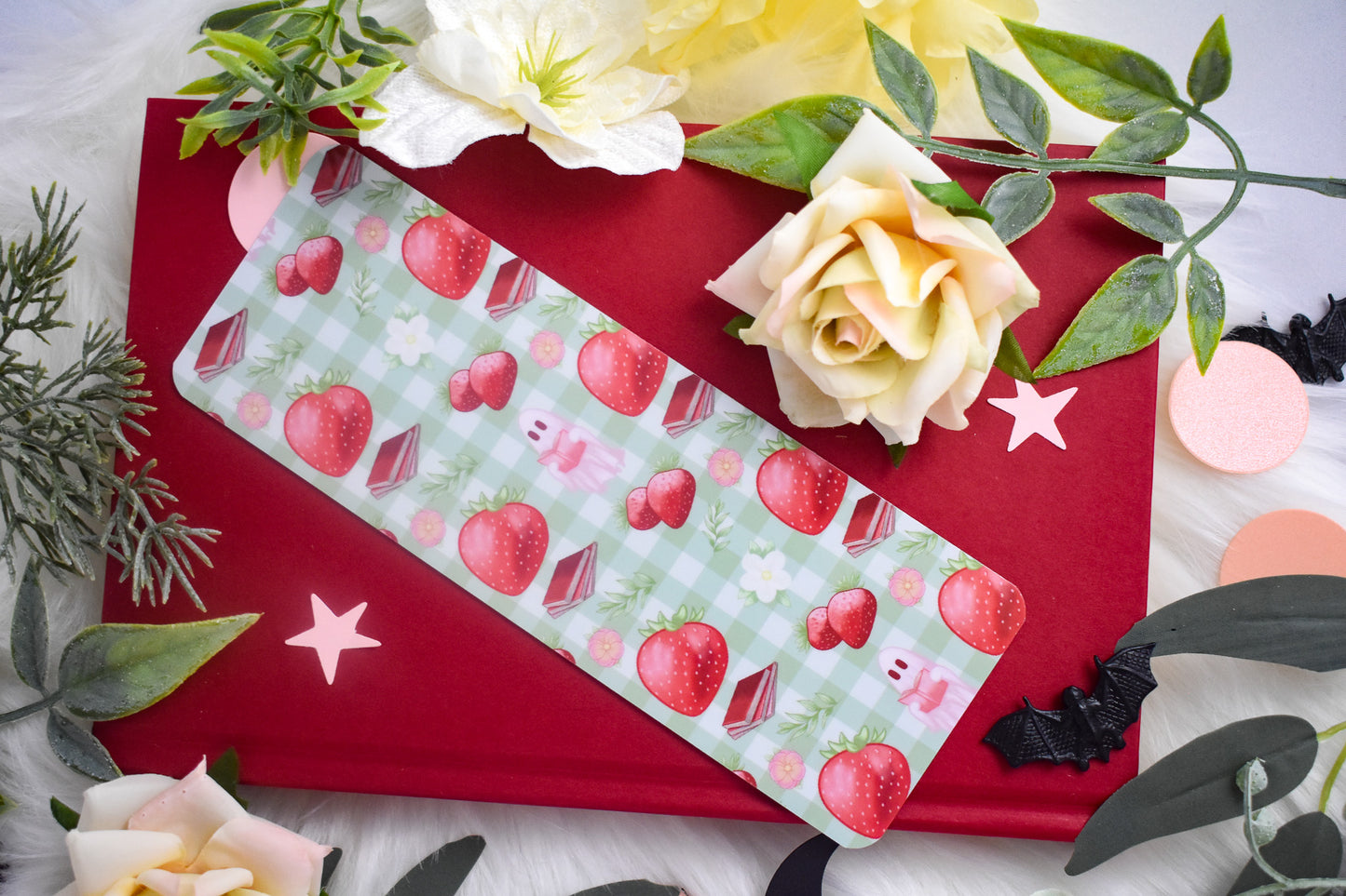 Bookmark with strawberry design on a red book with flowers and leaves.