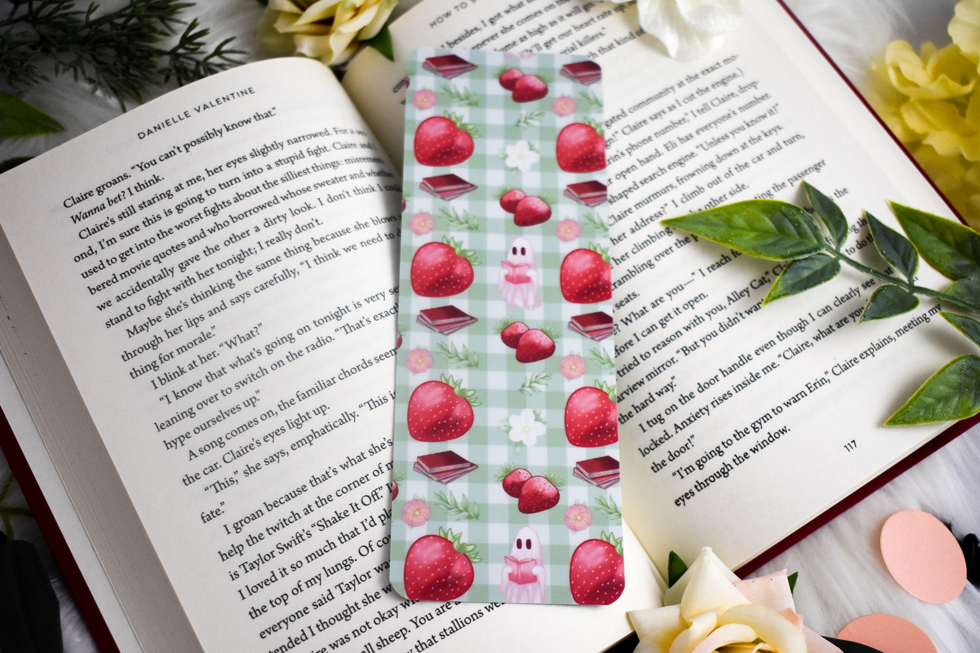 Book with a decorative bookmark featuring strawberries on a checkered background, surrounded by flowers and leaves.