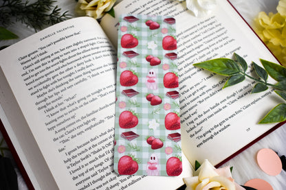 Book with a decorative bookmark featuring strawberries on a checkered background, surrounded by flowers and leaves.