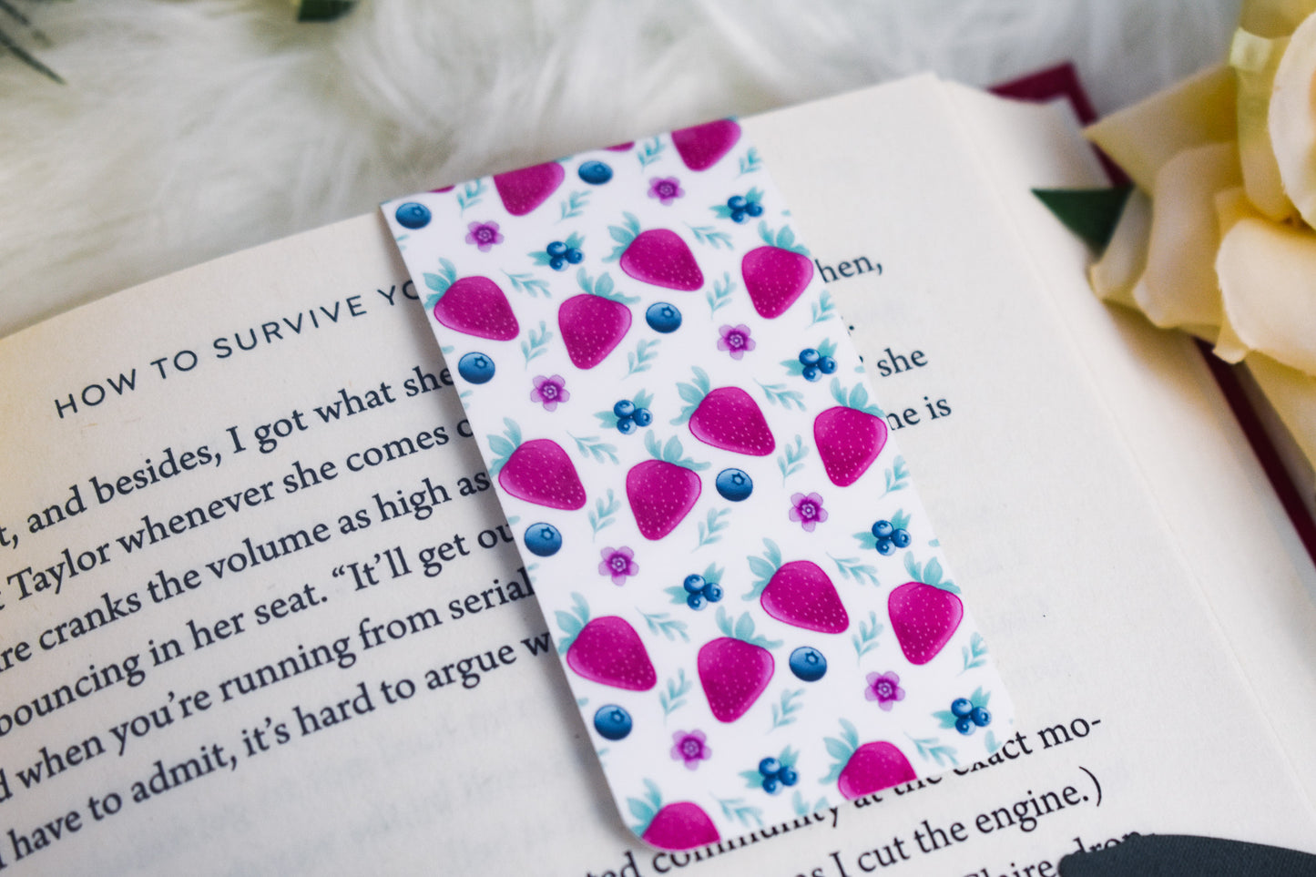 White bookmark with strawberry pattern on a book with a rose in the background