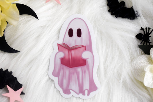 Ghost character holding a pink book on a textured white background with Halloween decorations.