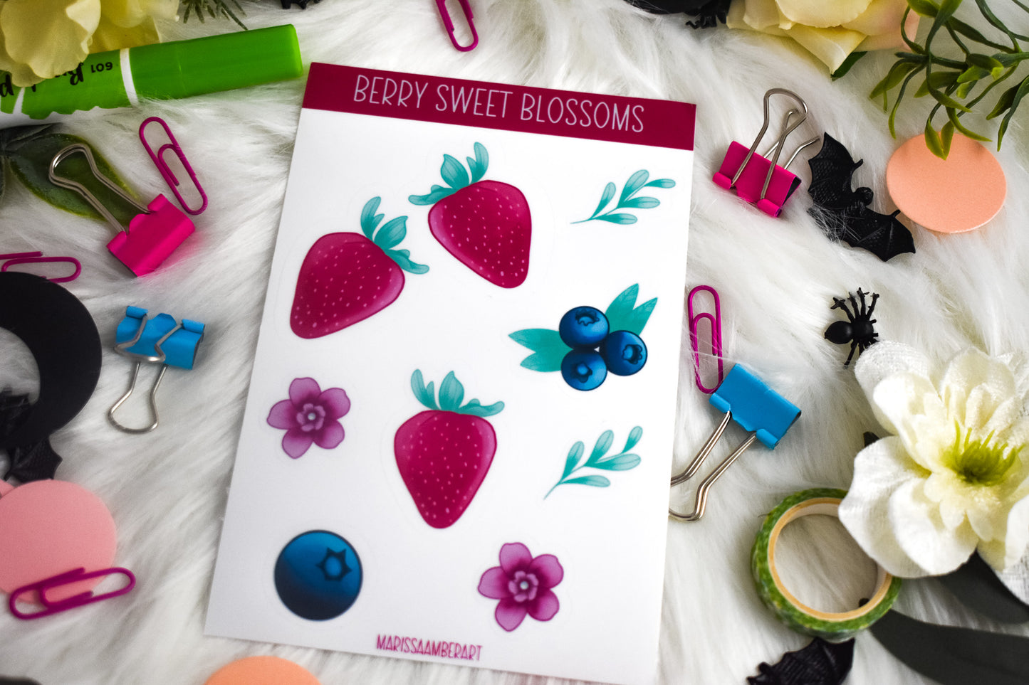 Sheet of decorative stickers with berries and flowers on a white surface with stationery items.