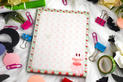 Notepad with colorful strawberry and ghost design surrounded by stationery items on a white surface