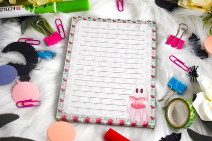 Notepad with lined paper surrounded by stationery items on a white surface