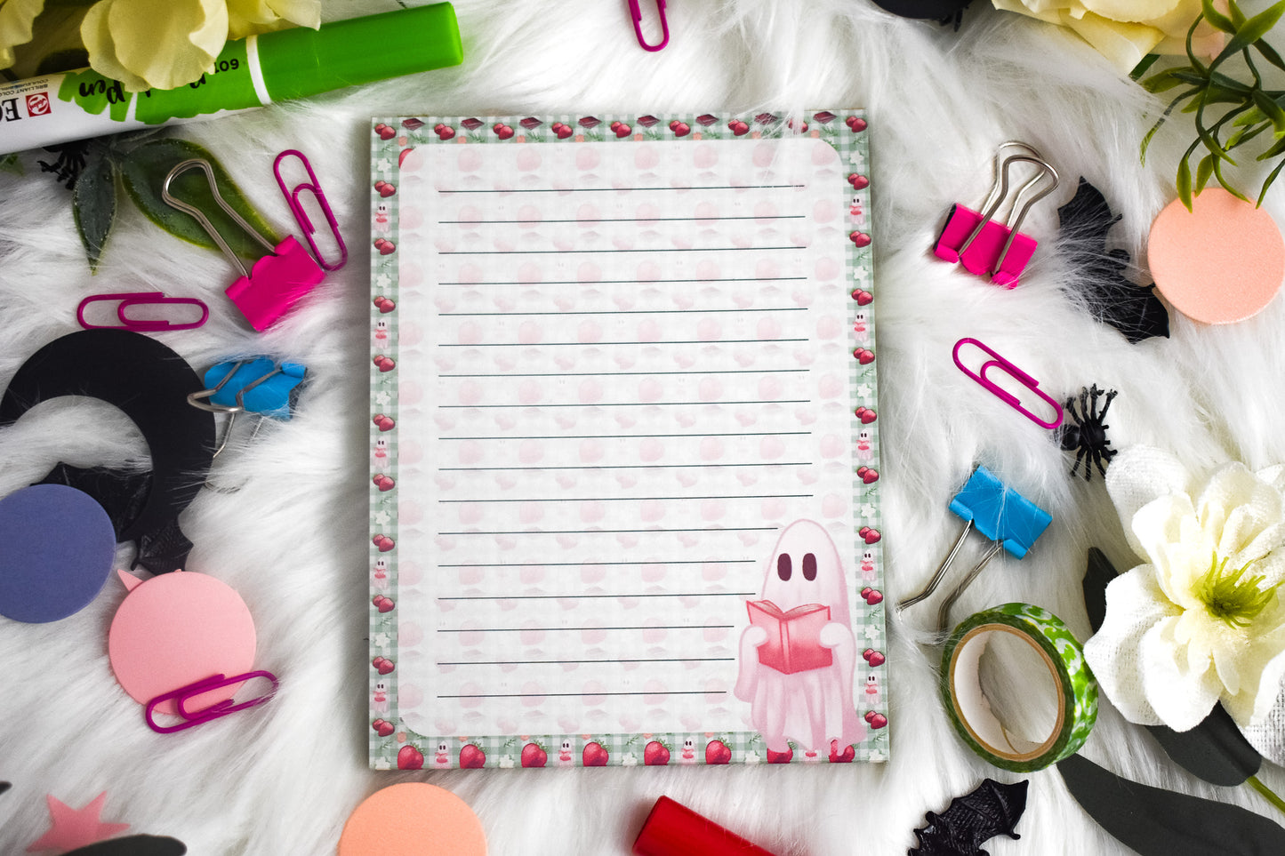 Notepad with lined paper surrounded by stationery items on a white surface
