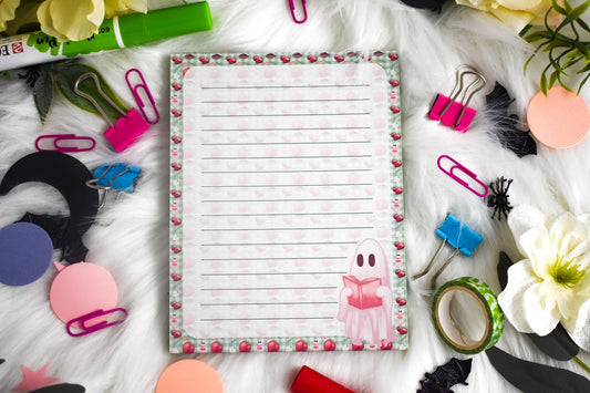Notepad with lined paper surrounded by stationery items on a white surface