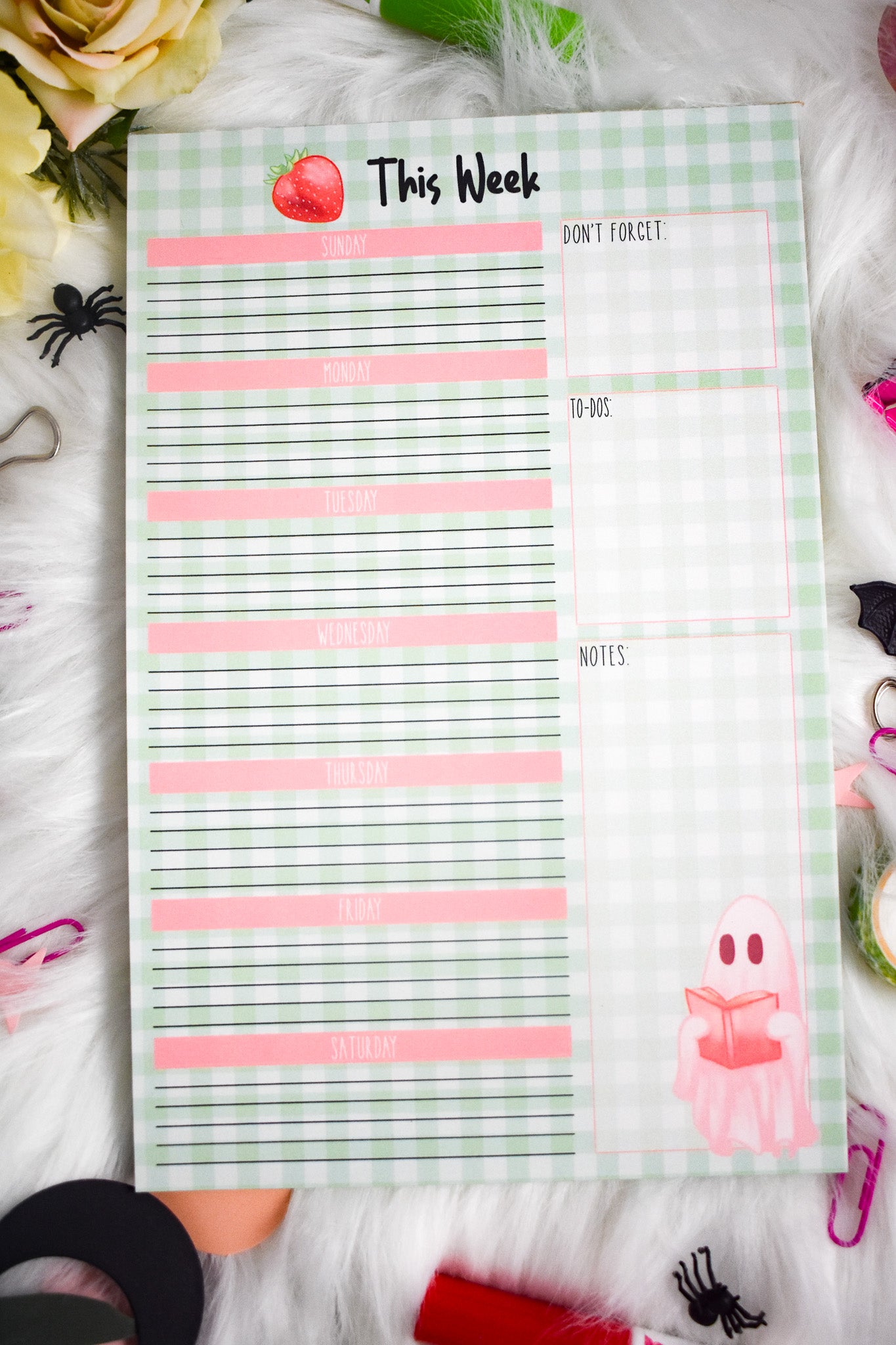 Weekly planner pad with Halloween-themed designs on a decorative surface with stationery items.