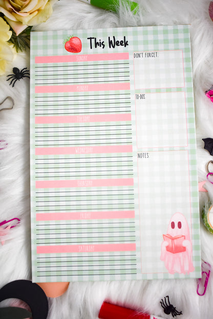 Weekly planner pad with Halloween-themed designs on a decorative surface with stationery items.