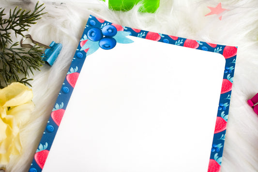Notepad with decorative border on a white surface with flowers and clips.