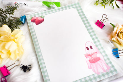 Notepad with a ghost illustration on a desk with flowers and stationery items