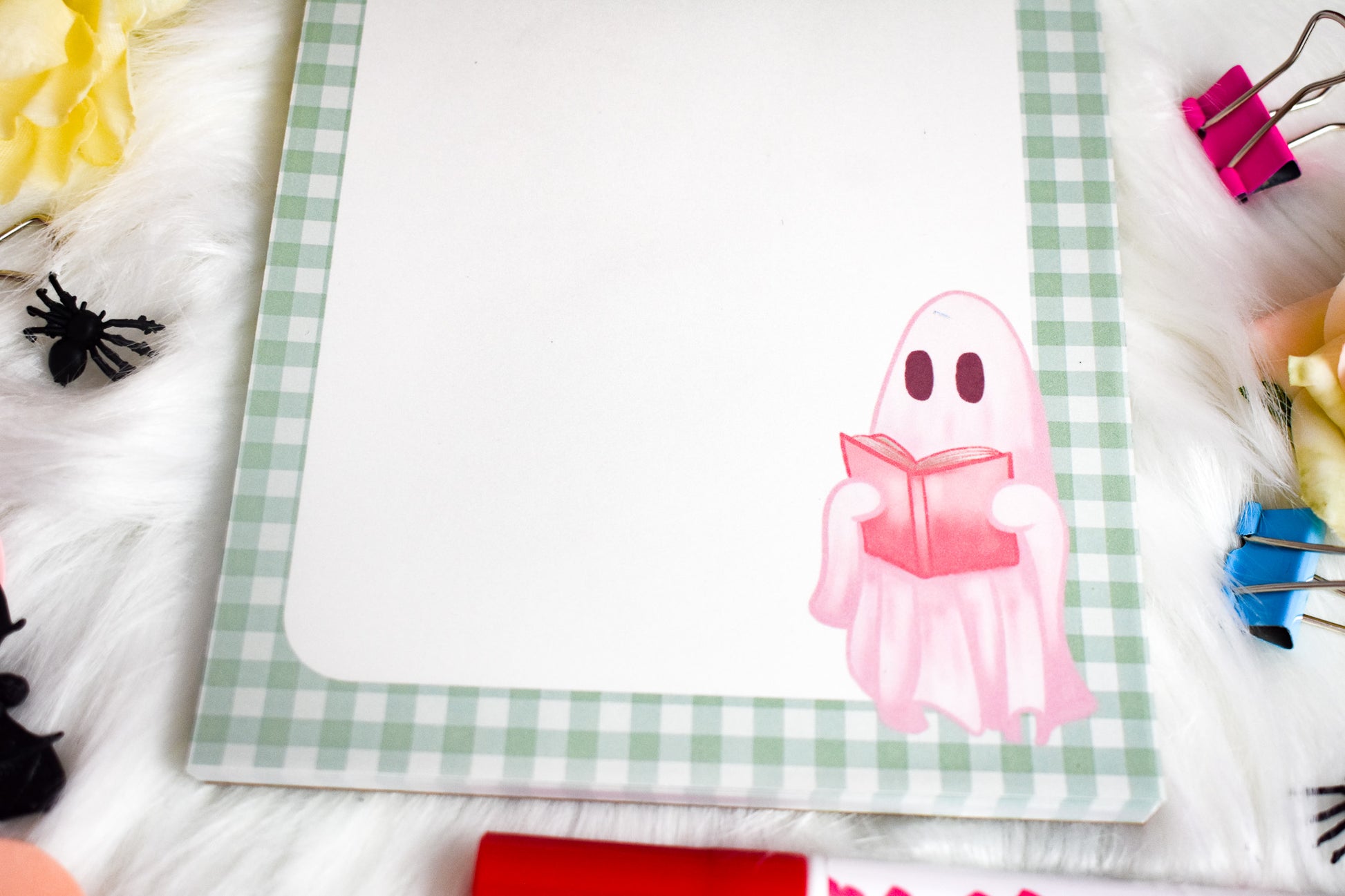 Notepad with a ghost illustration on a desk with flowers and stationery items