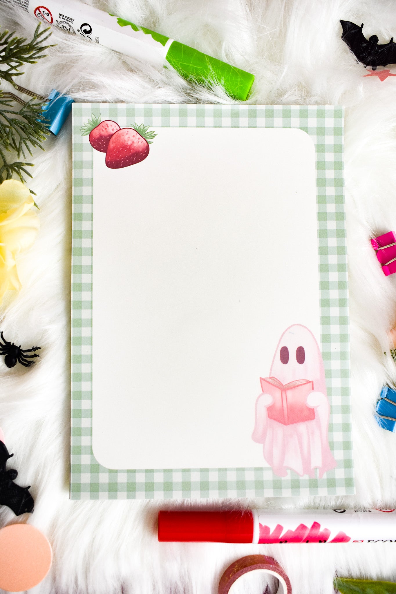Notepad with a ghost illustration on a desk with flowers and stationery items