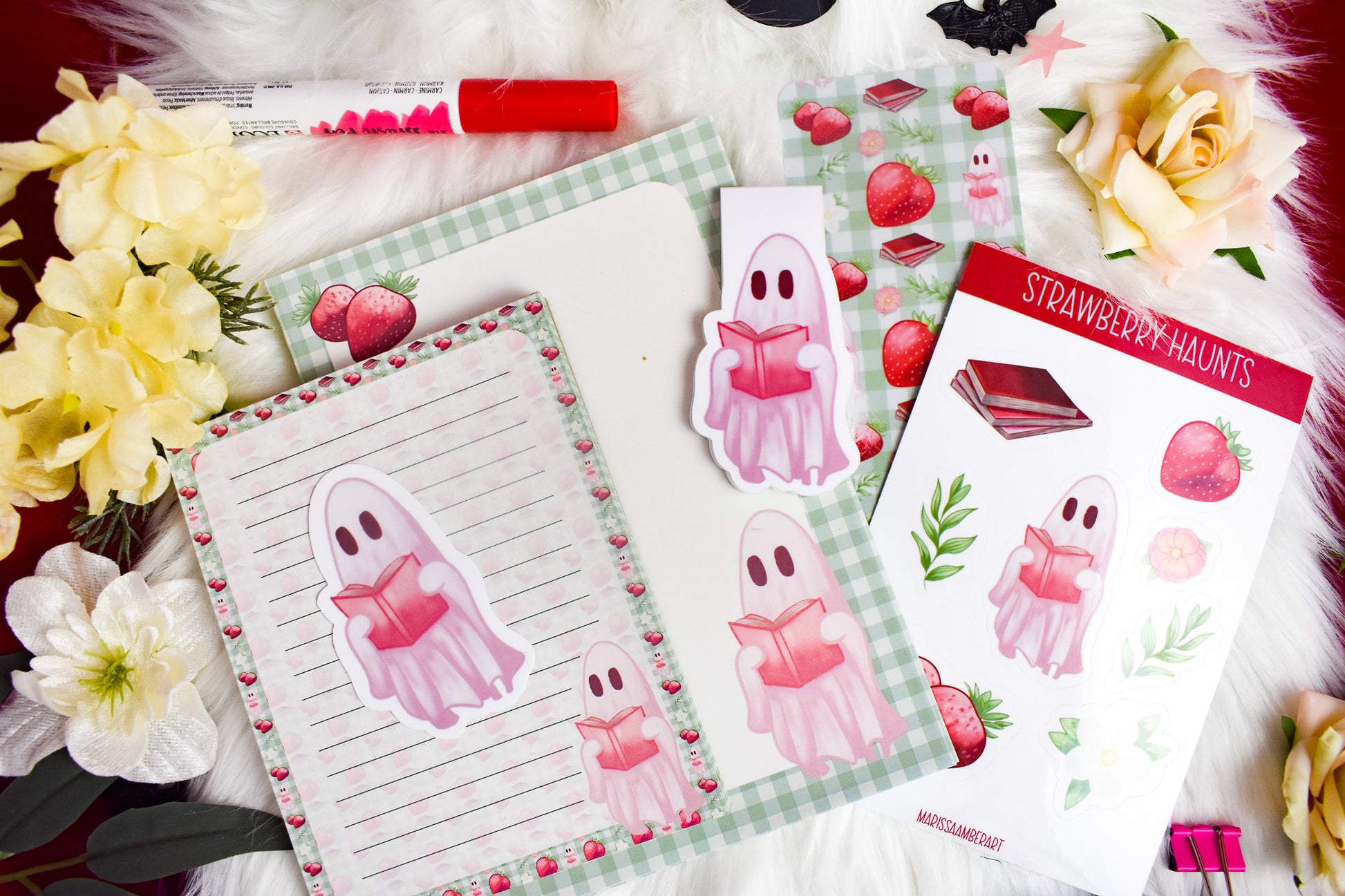 Die-cut sticker, die-cut magnetic bookmark, a lined notepad, a blank notepad, sticker sheet and traditional bookmark with ghost and strawberry designs on a white background