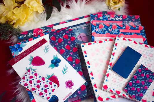 Collection of colorful planners and notebooks with floral and strawberry designs on a red surface.