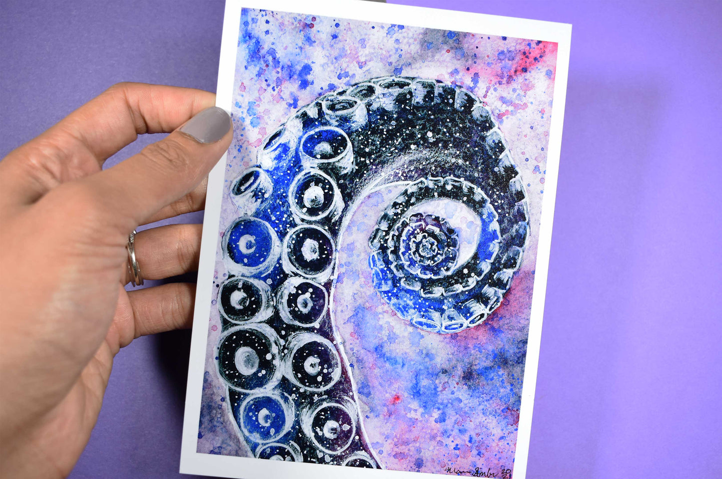 Hand holding a card with a blue and black spiral tentacle design against a purple background