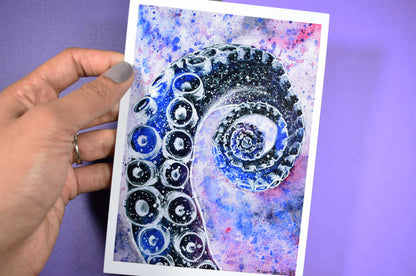 Hand holding a card with a blue and black spiral tentacle design against a purple background