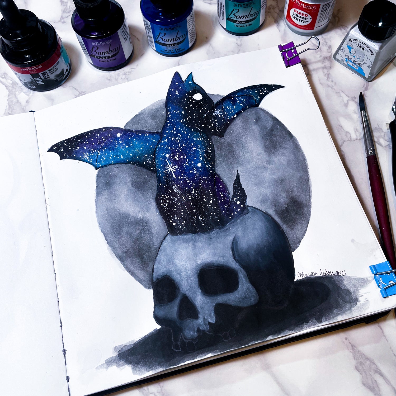Artistic depiction of a skull with a blue and black cat on a marble surface with art supplies.