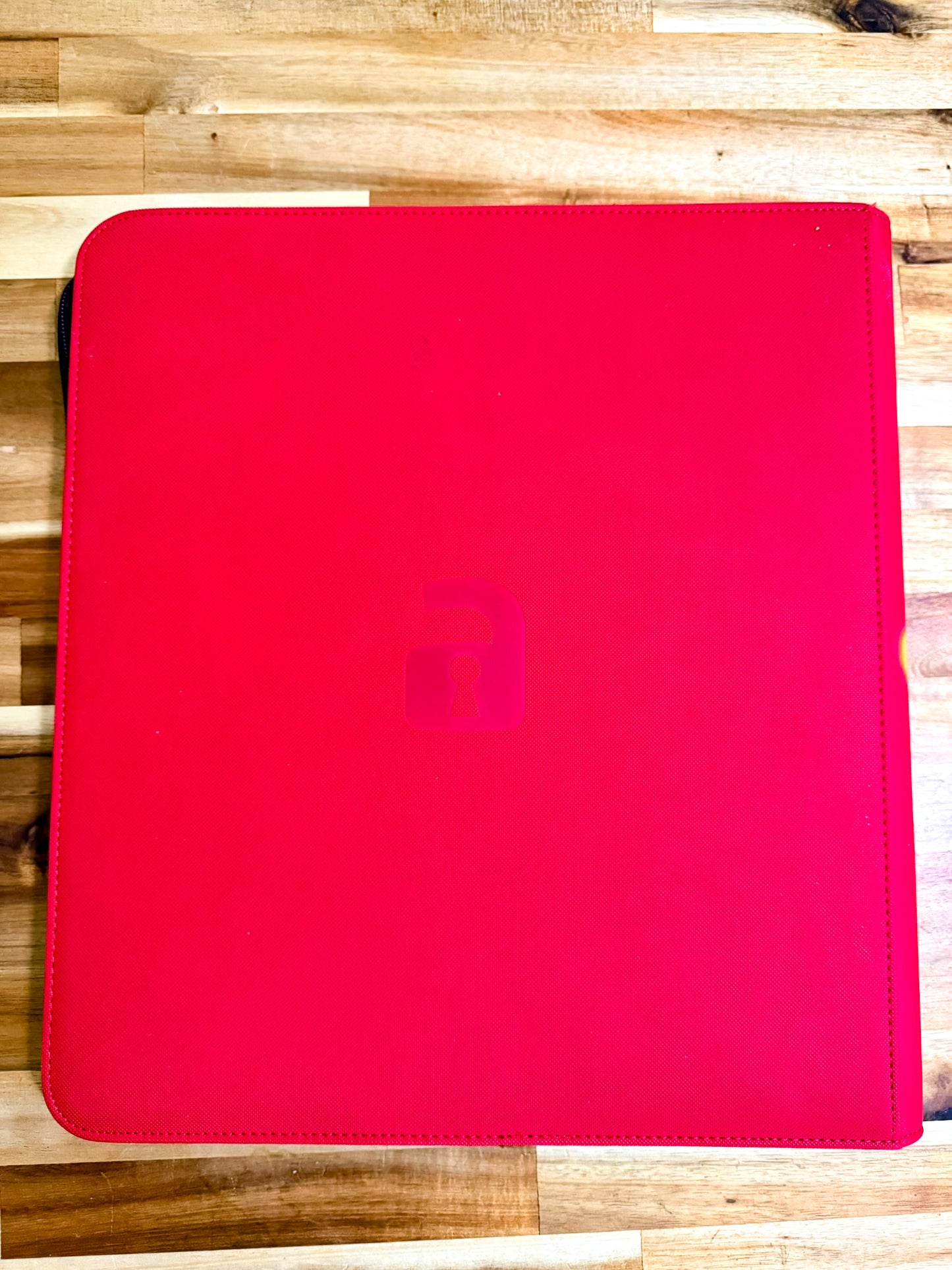 A bright red tablet sleeve or folio case with a subtle embossed lowercase 'lock' logo in the center, shown on a light wood plank surface.