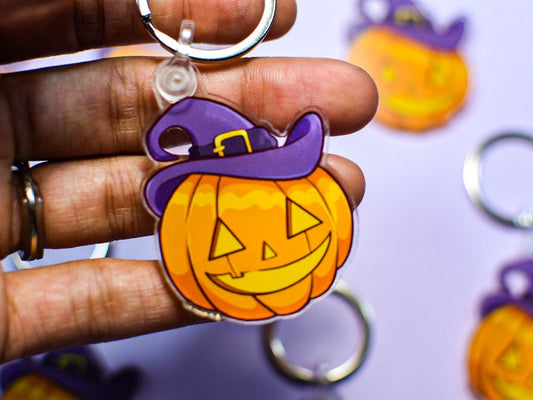 Halloween-themed keychain with a pumpkin and witch hat held by a hand.