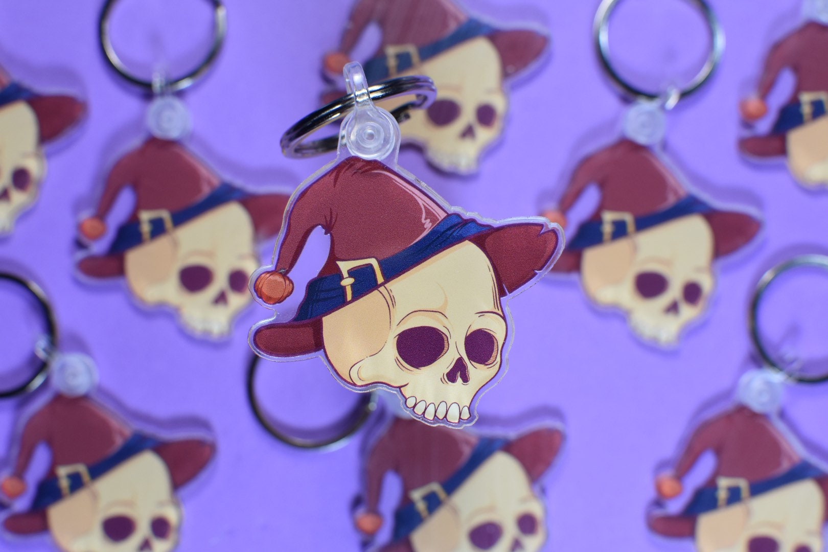 Keychain with skull design wearing a red witches hat on a purple background
