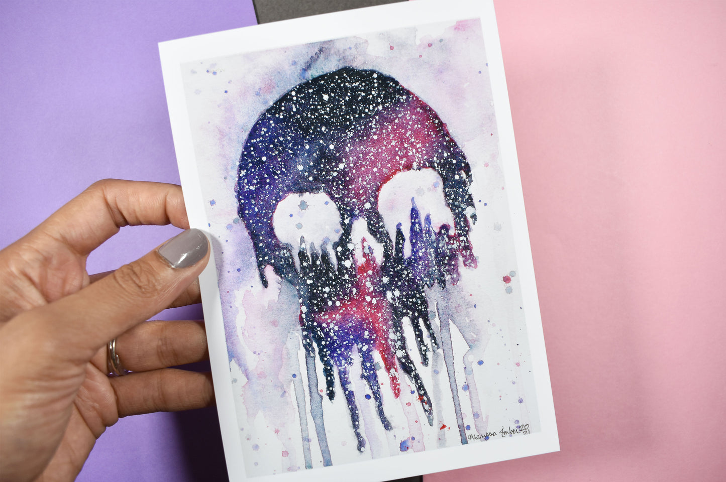 Hand holding a card with a watercolor design of a city skyline under a starry night sky.