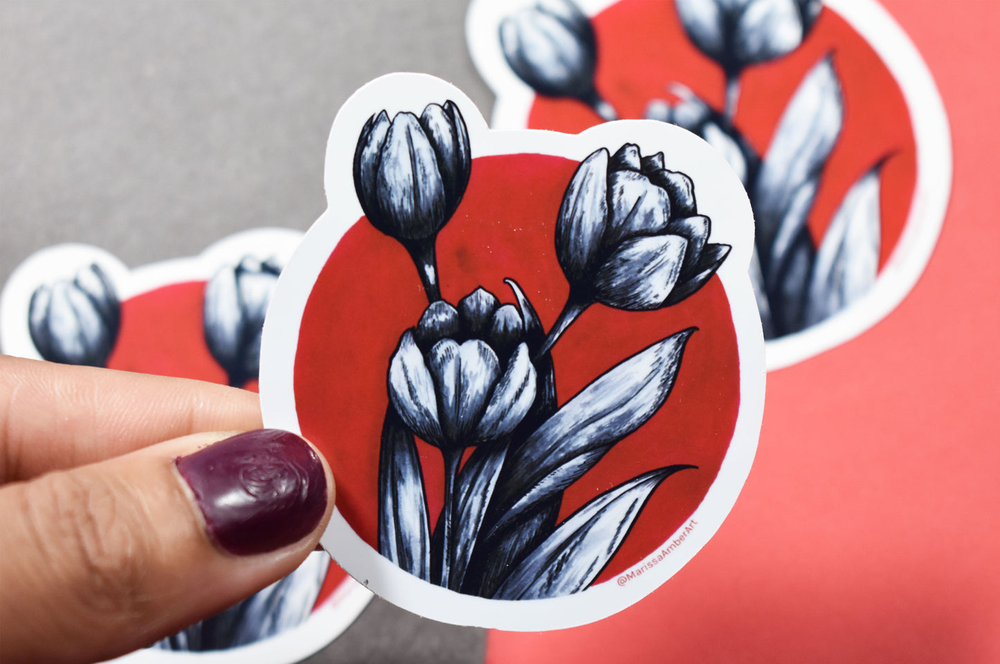 Sticker with black tulip design on a red background held by a hand.