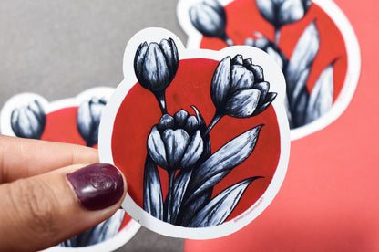 Sticker with black tulip design on a red background held by a hand.